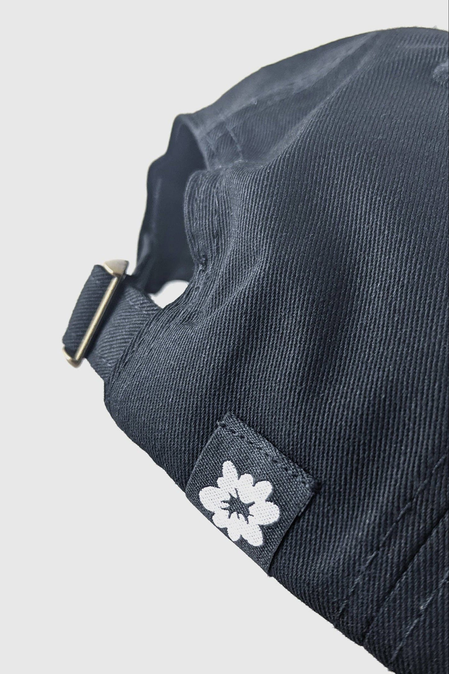 Close up of the back of the Boom Boom Hat by Badaboöm Studio, featuring an embroidered graphic of an explosion on a black baseball cap, set against a light grey background.