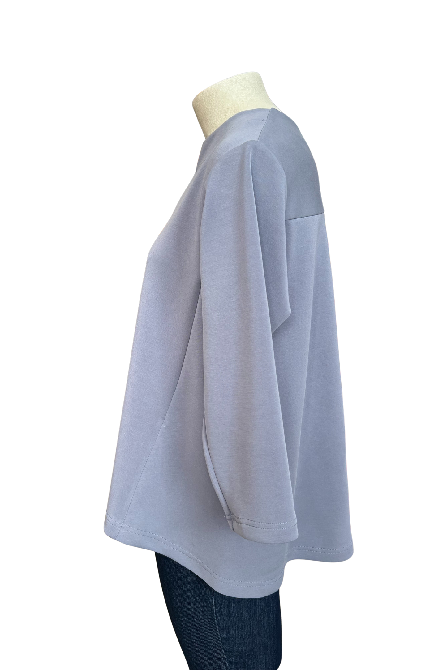 A side view of the Vanessa Top by Solomia in Blue is shown on a mannequin against a white background. It has a notched neckline, 3/4 sleeves, a rounded hi-low hemline, and a vertical seam down the front.