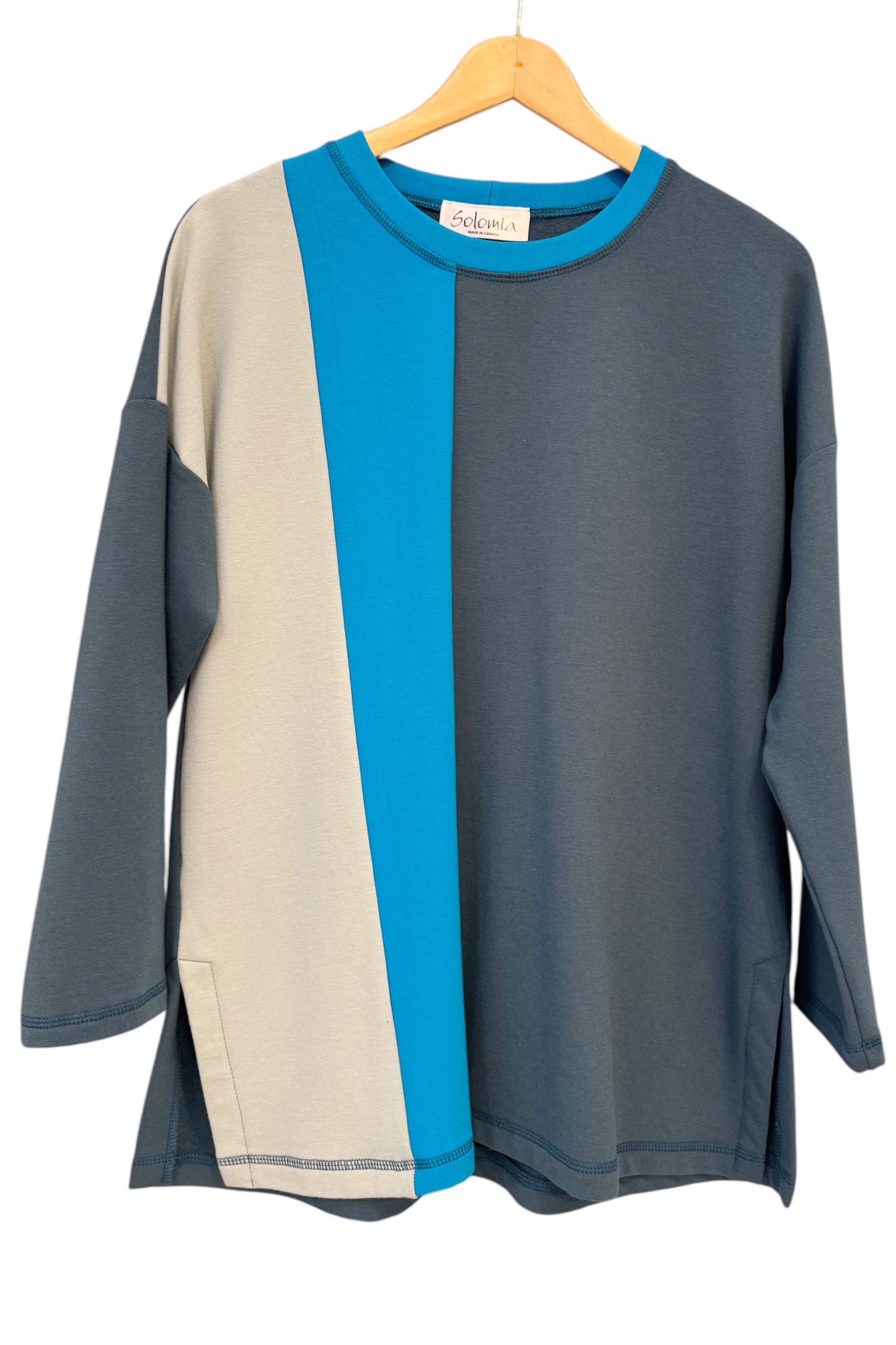The Dora Sweater by Solomia in Teal/Blue, a colour-blocked top featuring a round neckline, long sleeves, and a relaxed fit, is shown against a white background.