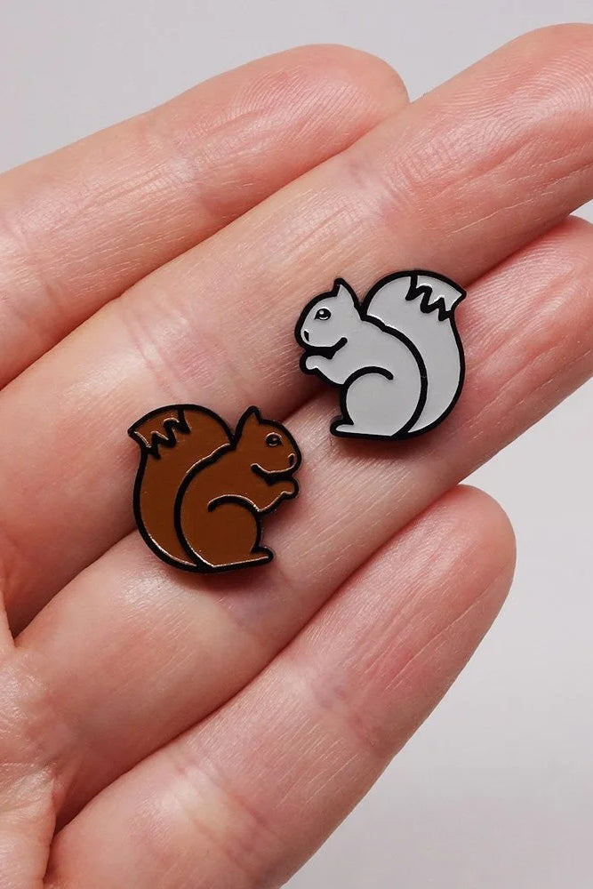 Two Lillipop squirrel-shaped earrings held between fingers against a neutral background