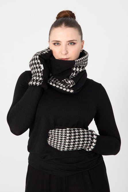 A woman wearing the Slak A-25 mittens in Black and White Houndstooth and a matching scarf with a black outfit.