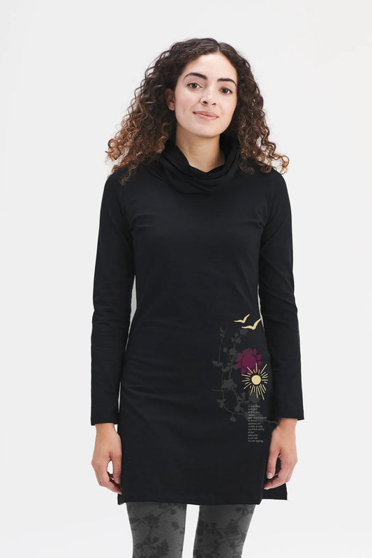 A woman wearing the Oléana Tunic Dress by Message Factory, with a cowl neck, long sleeves, nature-inspired print decal on the left hip, and French quote. She is wearing it with grey floral leggings against a white background