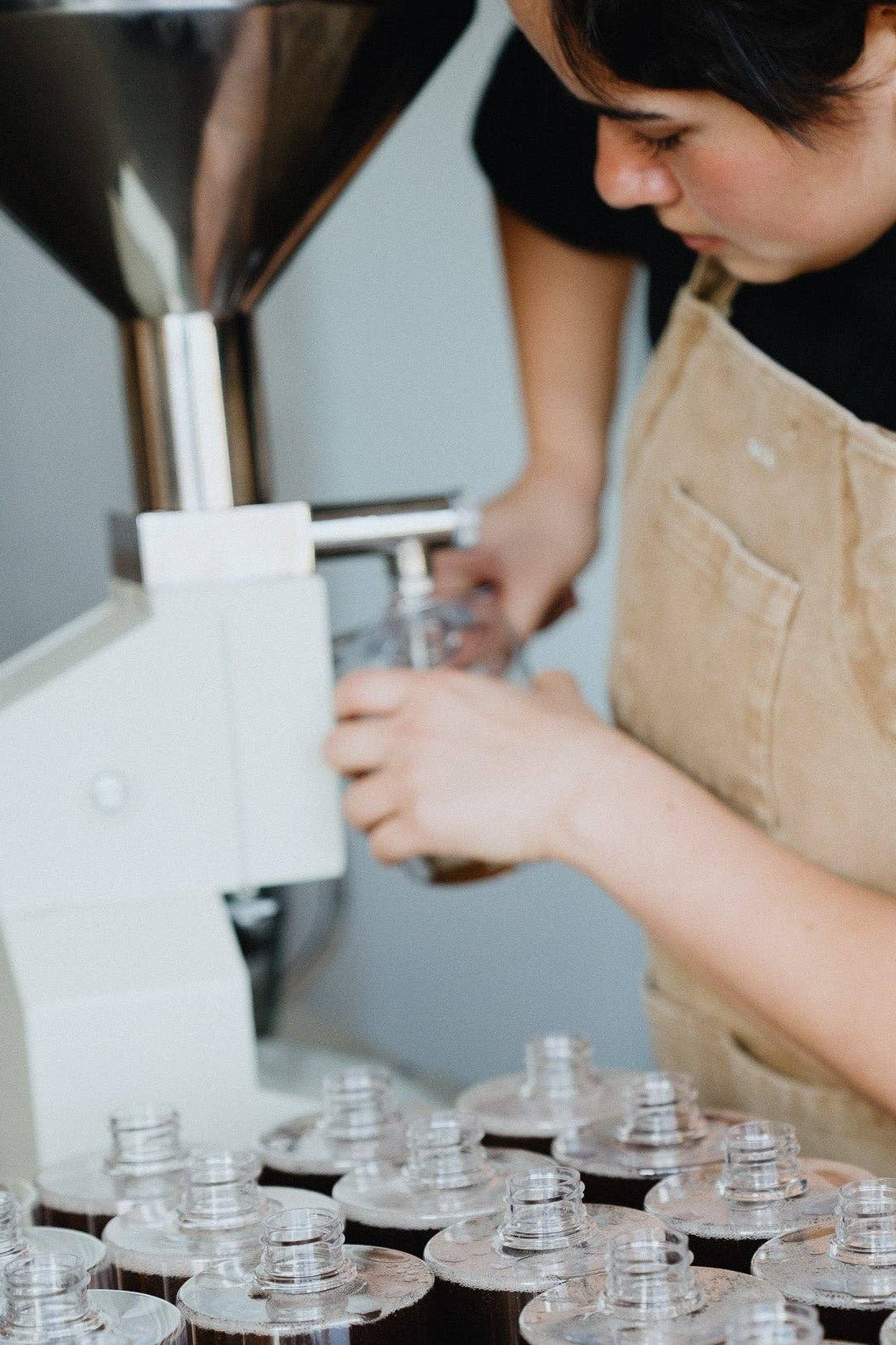 Person in a beige apron operating a machine with multiple soap bottles on a counter.