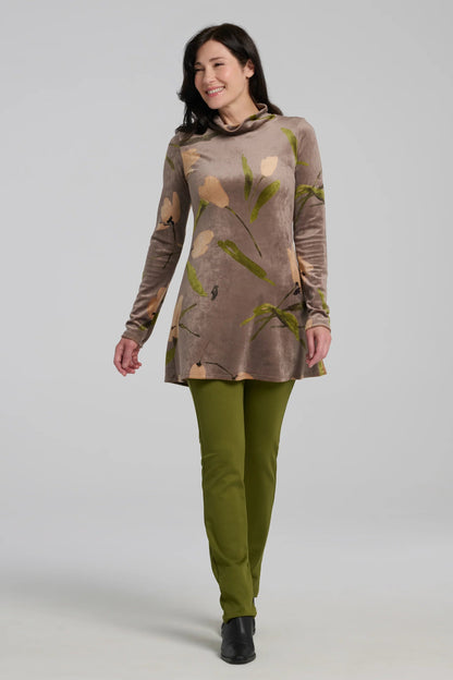 A woman wearing the Holly Tunic by Kollontai in Taupe, an Italian velvet A-line tunic with a turtleneck, long sleeves, and a floral print. She is wearing it with the Bari Pants in Green and standing in front of a grey background. 