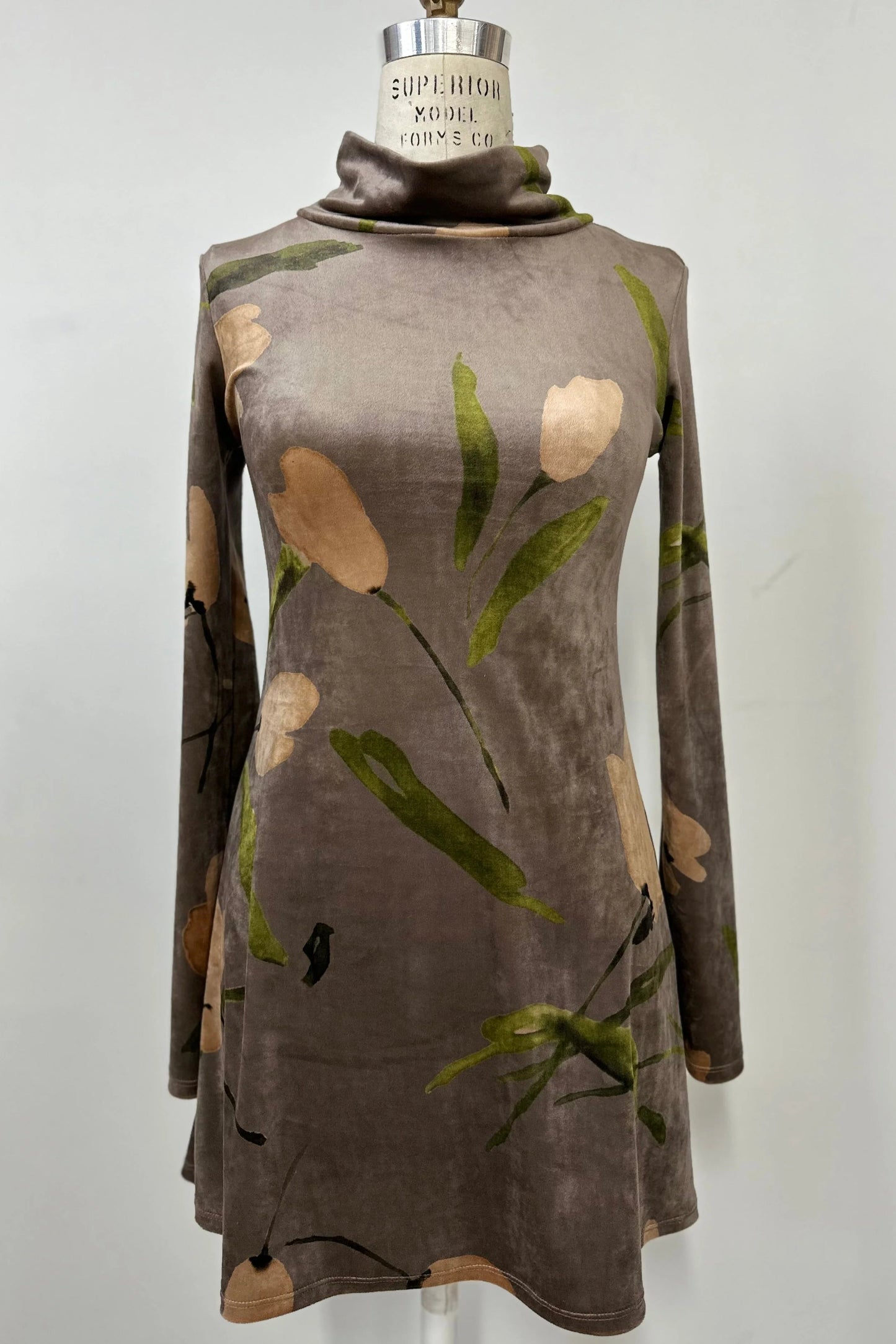 The Holly Tunic by Kollontai in Taupe, an Italian velvet A-line tunic with a turtleneck, long sleeves, and a floral print, is shown on a mannequin against a  a grey background. 