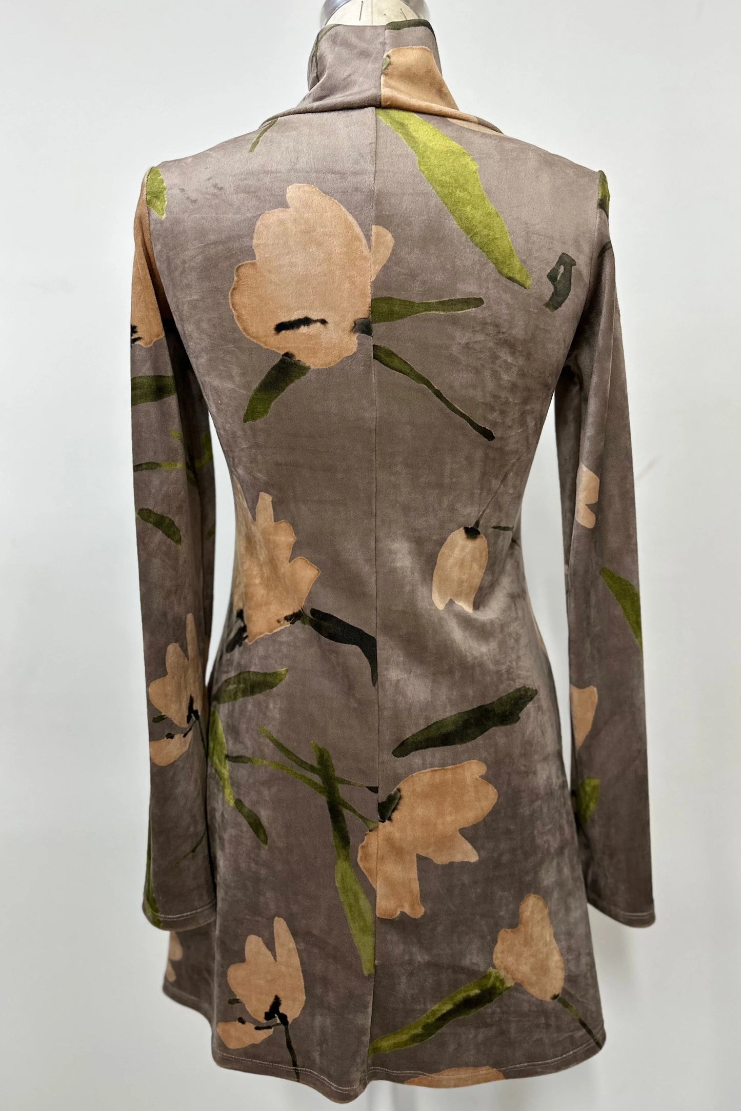 A back view of the Holly Tunic by Kollontai in Taupe, an Italian velvet A-line tunic with a turtleneck, long sleeves, and a floral print, is shown on a mannequin against a  a grey background. 