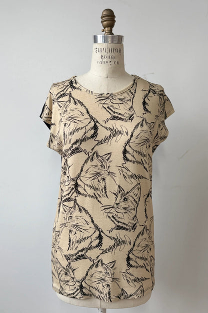 The Arto Tunic by Kollontai in Cats/Beige Print is shown on a mannequin against a grey background. It has a round neck, short extended sleeves, and a straight cut with a solid black back. 