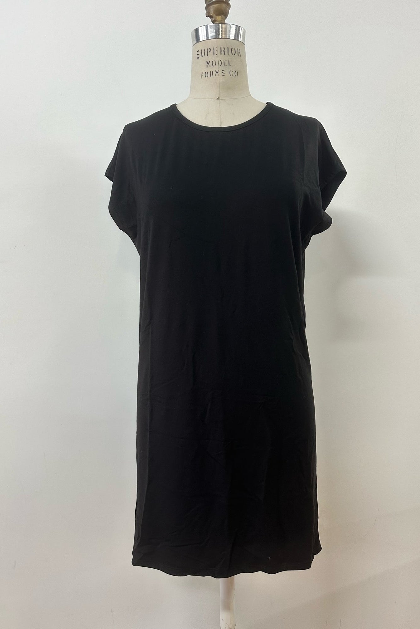 The Arwen Dress by Kollontai in Black, a t-shirt dress with a round neck, short extended sleeves, a loose ft, and an above the knee hem, is shown on a mannequin in front of white background. 