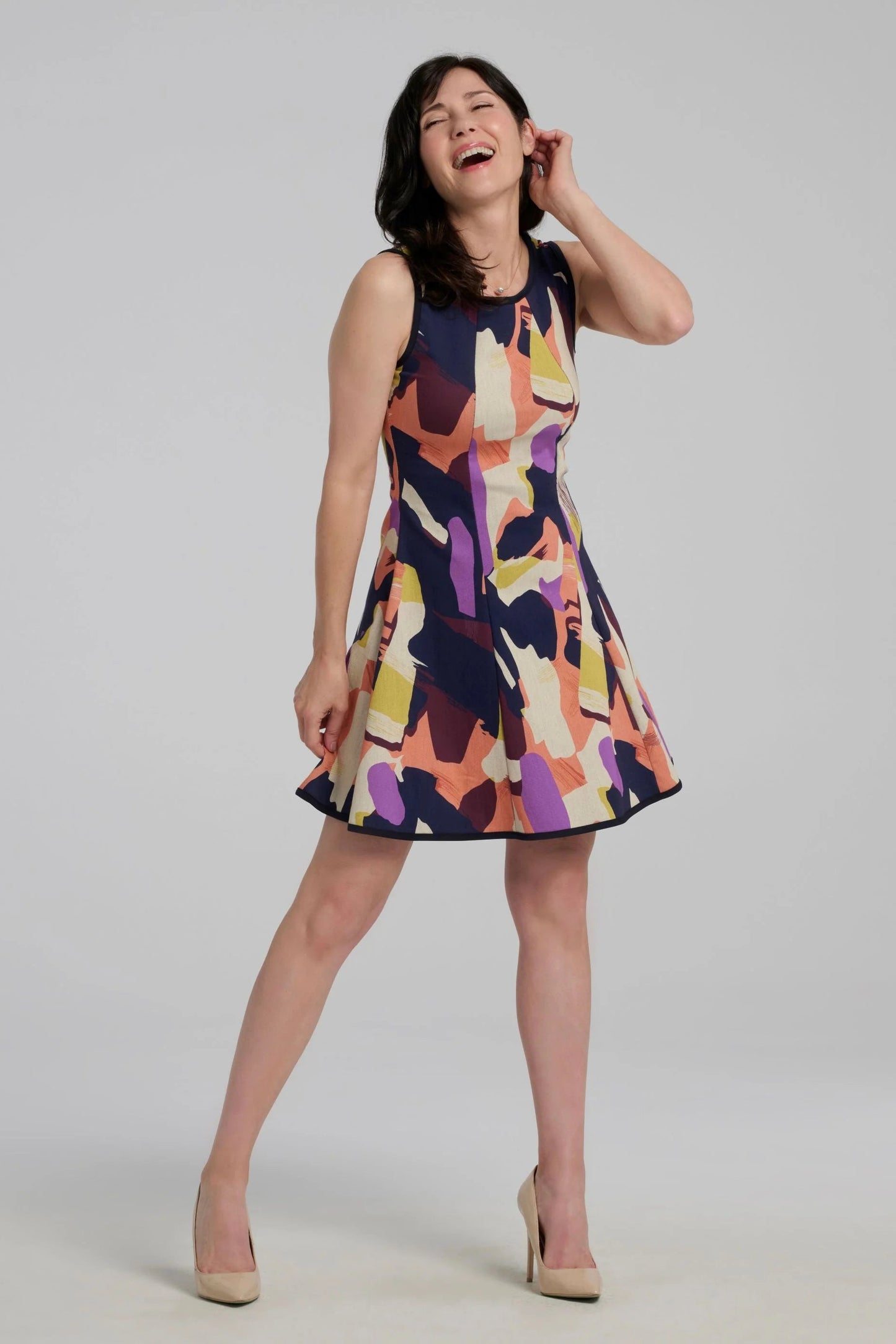 A woman wearing the Silba SS26 Dress by Kollontai, a sleeveless short dress in a Multicolour abstract print with a fit and flare shape and princess seams. She is standing in front of a plain background. 