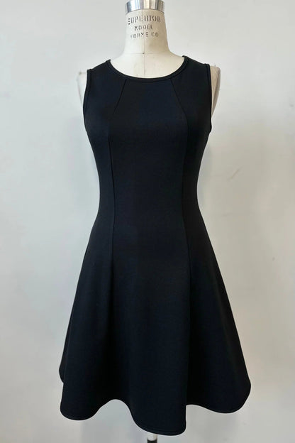 The Toscana Dress by Kollontai in Black, a sleeveless piece with a round neck, princess seams, and fit and flare shape with a full skirt that hits above the knee, is shown on a mannequin against a white background. 