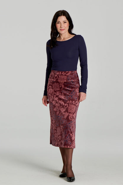 A woman wearing Winslet Skirt by Kollontain in Burgundy paisley velvet,  a 7/8 length A-line pull-on skirt. She is wearing it with a navy top and standing in front of a white background