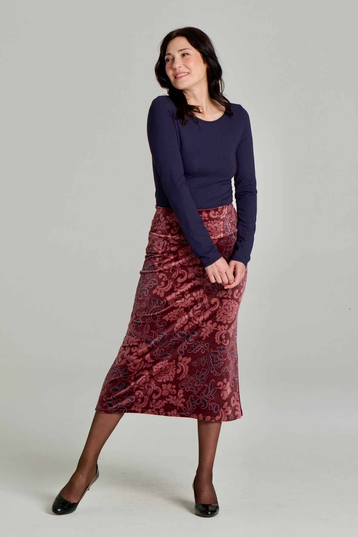 A woman wearing Winslet Skirt by Kollontain in Burgundy paisley velvet,  a 7/8 length A-line pull-on skirt. She is wearing it with a navy top and standing in front of a white background