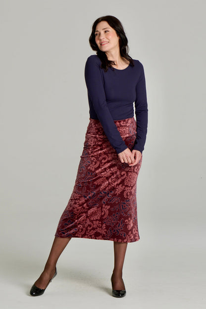 A woman wearing Winslet Skirt by Kollontain in Burgundy paisley velvet,  a 7/8 length A-line pull-on skirt. She is wearing it with a navy top and standing in front of a white background