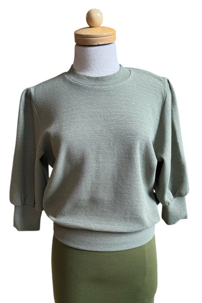 The Bridge Sweater by Allison Wonderland in Matcha, featuring elbow length sleeves and a ribbed neckline, cuff, and hem, is shown on a mannequin against a white background. 