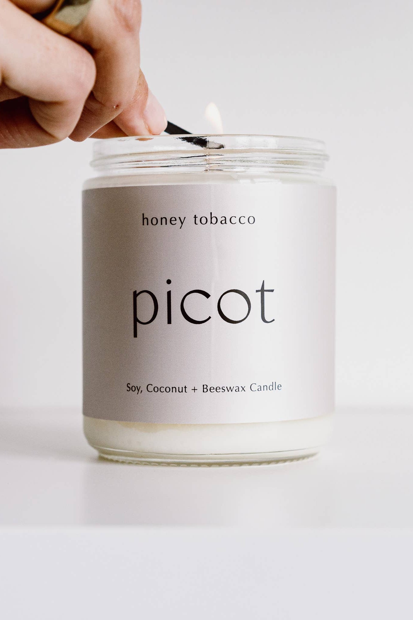 Person lighting a Picot honey tobacco candle with a lighter on a white background
