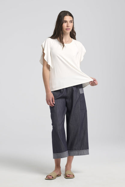 A woman wearing the Morwenna Pants from Kollontai, lightweight denim pants with wide cropped legs, an elastic waist, and contrasting trim on the large patch pockets and the cuffs. She is wearing them with the Morgana T-Shirt in white and is standing in front of a white background. 