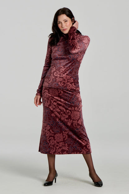 A woman wearing the Everdeen Sweater by Kollontai, a velvet turtleneck in Burgundy paisley print. She is wearing it with the matching Winslet Skirt, a 7/8 A-line pull-on skirt, and standing in front of a white background