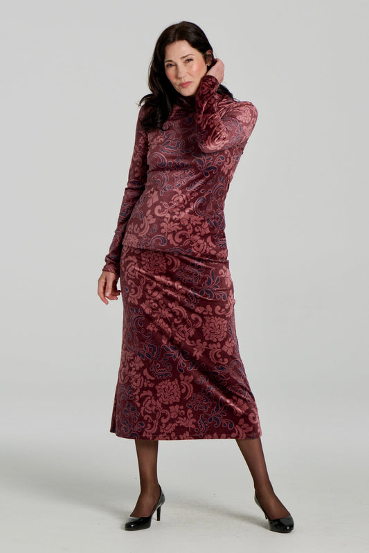A woman wearing the Everdeen Sweater by Kollontai, a velvet turtleneck in Burgundy paisley print. She is wearing it with the matching Winslet Skirt, a 7/8 A-line pull-on skirt, and standing in front of a white background
