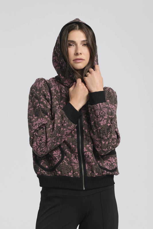 A waist up view of a woman wearing the Katniss Jacket by Kollontai in Pink, a bomber style jacket in jacquard fabric with a corduroy lined hood and rounded patch pockets 