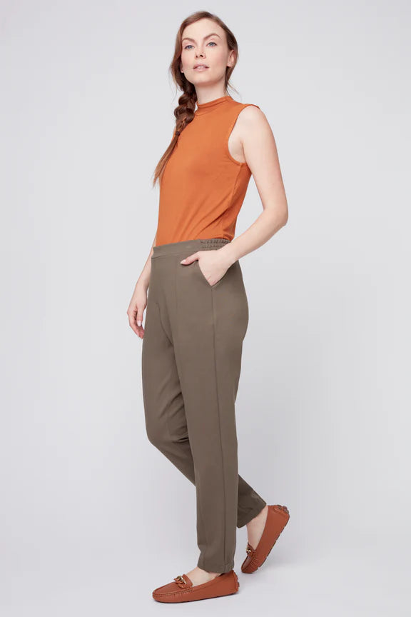 Side view of a woman wearing the Sarah Cigarette Pant by Julei in Fern featuring four way stretch fabric, pin tucks for shape, and a pull-on waist. She is wearing them with an orange shirt and standing in front of a white background. 