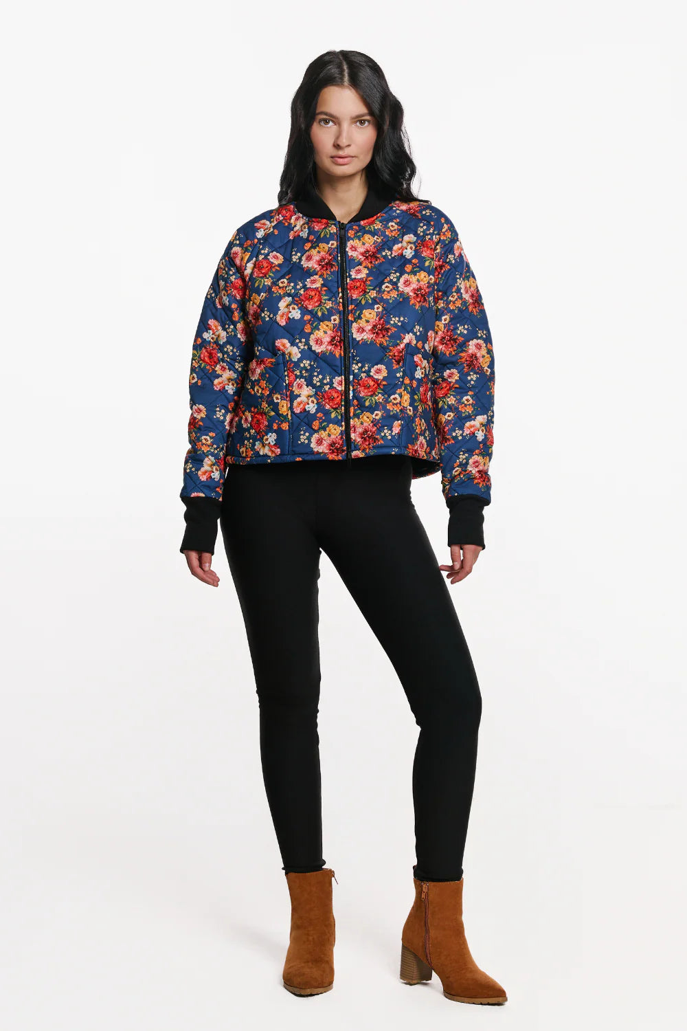 A woman wearing the Harper Bomber Jacket by EMK, a floral bomber jacket in quilted fabric with black waffle knit fabric at the cuffs and collar. She is wearing it with black pants and standing in front of a white background. 