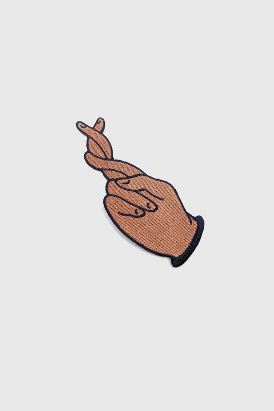 The Twist Patch by Badaboöm Studio, showing extra long crossed fingers, is shown against a white background. 