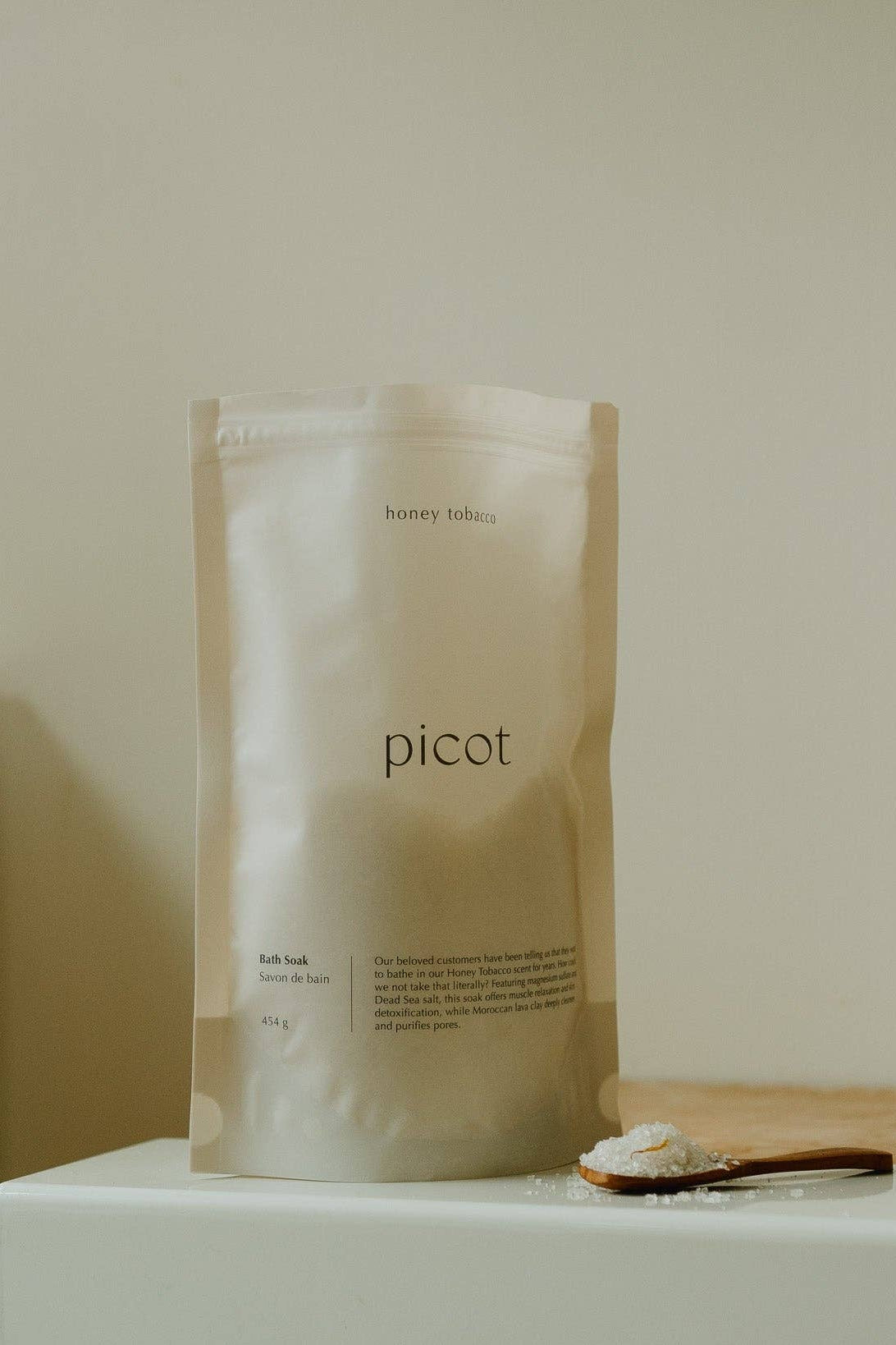 A bag of Picot's Honey Tobacco bath soak, shown with a scoop and salts on a bathroom counter.