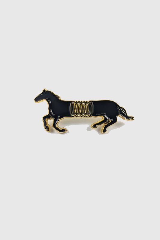The Spring Horse Pin by Badaboöm Studio, featuring a black horse with a gold spring in the mid-section, is shown against a white background. 