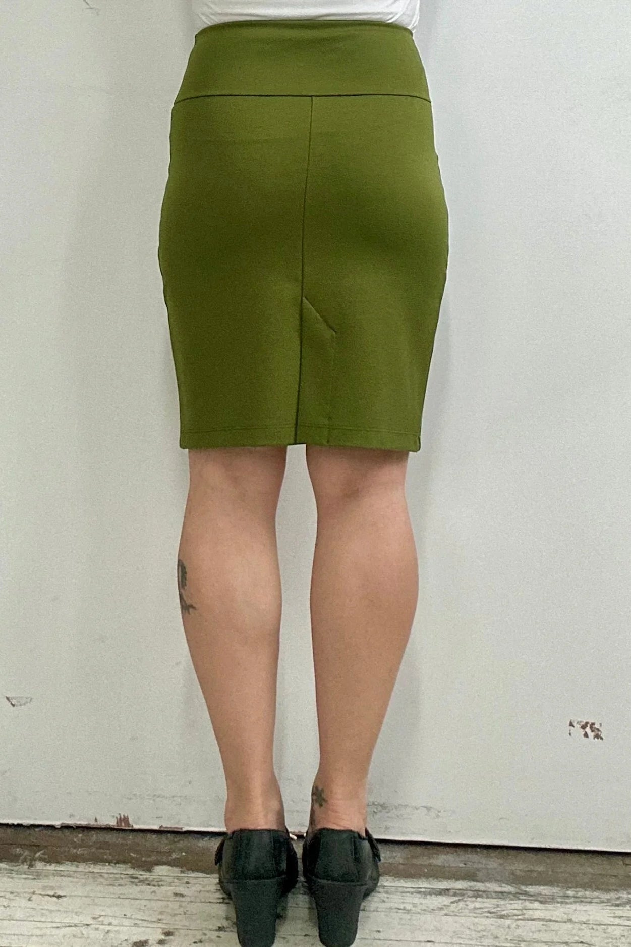 Waist down back view of a woman wearing the Veneto Skirt by Kollontai in Granny Smith, a pencil skirt with a wide-pull on waistband, back slit, and hem that hits above the knee.