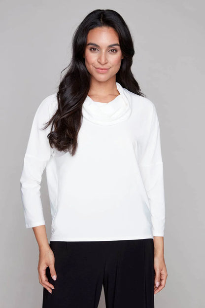 A woman wearing the Perry Top by Compli K in Ivory, featuring a cowl neck, 3/4 drop sleeves, and decorative buttons up the back. She is wearing it with black pants and standing in front of a white background. 