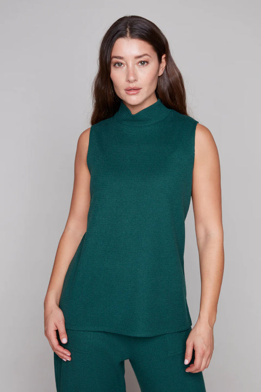 3/4 view of a woman wearing the Pascale Mock Neck Tank by Compli K in Forest Green, a long sleeveless top in a textured knit. She is wearing it with the matching Penelope pants and standing in front of a grey background. 