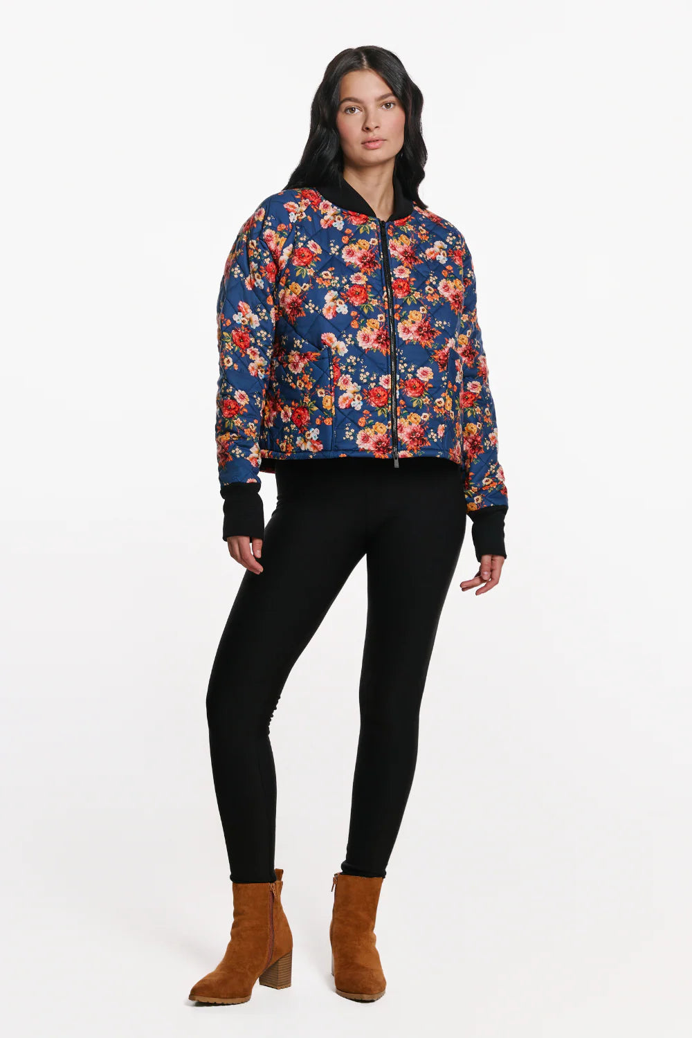 A woman wearing the Harper Bomber Jacket by EMK, a floral bomber jacket in quilted fabric with black waffle knit fabric at the cuffs and collar. She is wearing it with black pants and standing in front of a white background. 