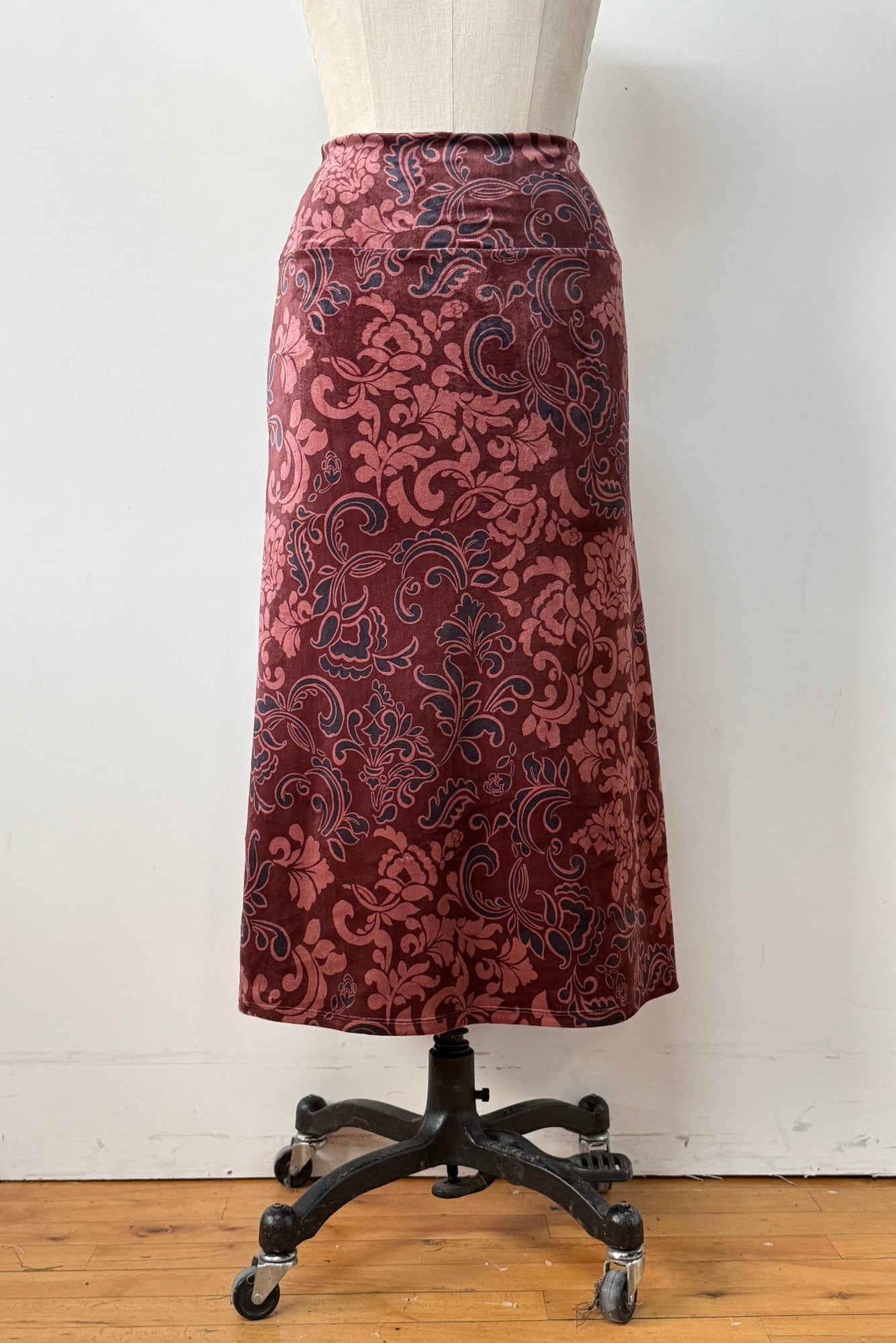 Back view of the Kollontai Winslet skirt, a burgundy velvet midi skirt, is shown on a mannequin against a white background. 