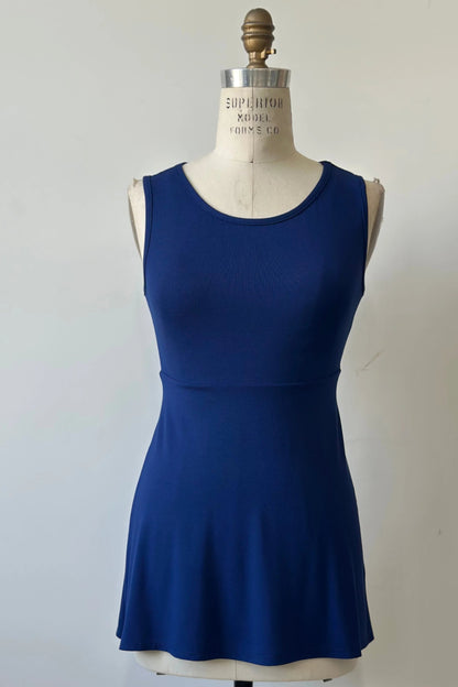 The Nira Top by Kollontai in Admiral blue, a sleeveless top with a wide neck, an empire waist, and a cut that's fitted through the bodice and flares away from the torso, is shown on a mannequin against a white background. 