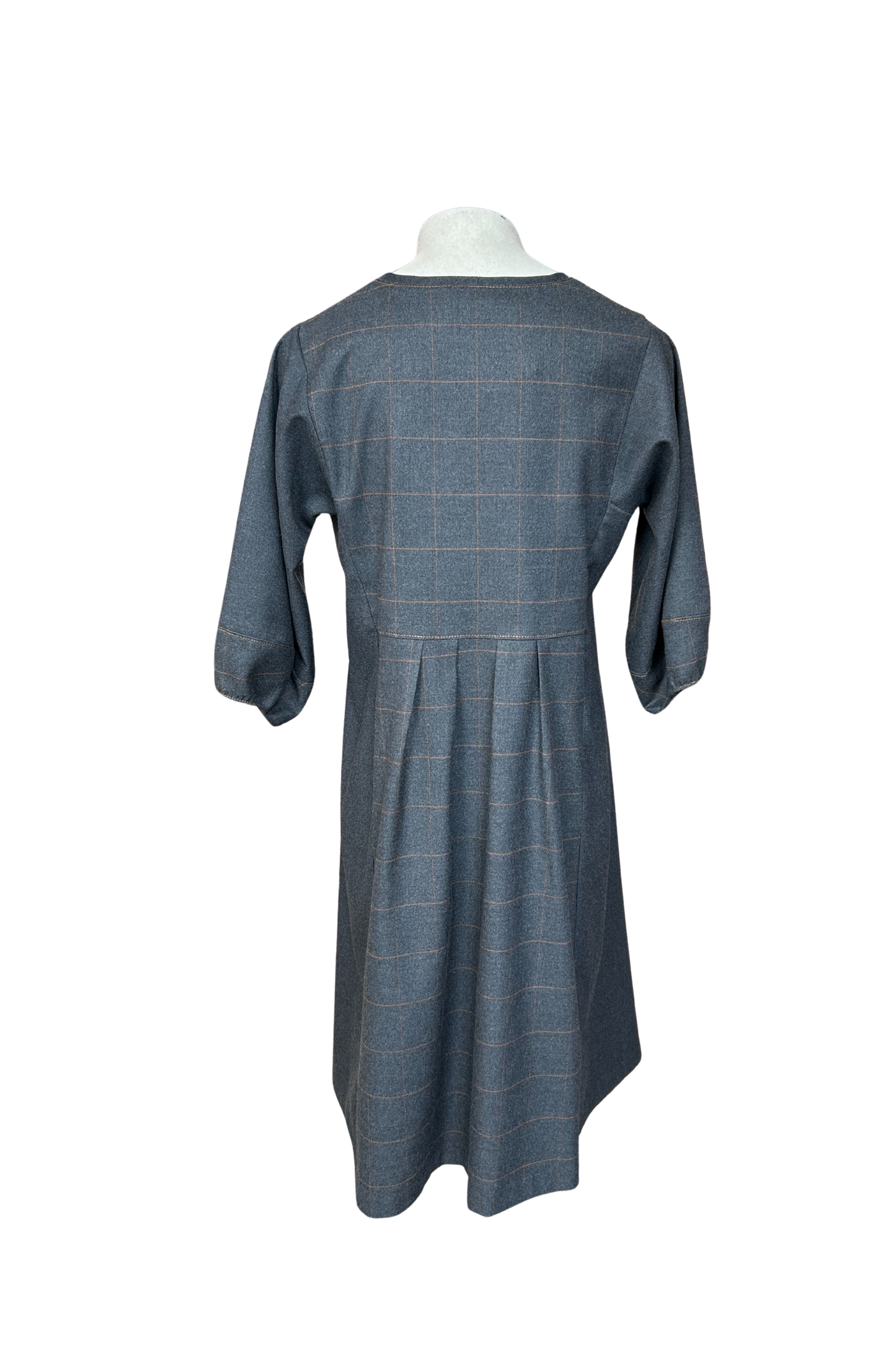 A back view of the Hanna Dress by Solomia in Grey is shown on a mannequin against a white background. This knee length dress has uniquely placed pleats and seams to create an architectural shape, with 3/4 length sleeves with structured cuffs. It has checked fabric on the front, back and cuffs, and solid grey fabric at the sides. 