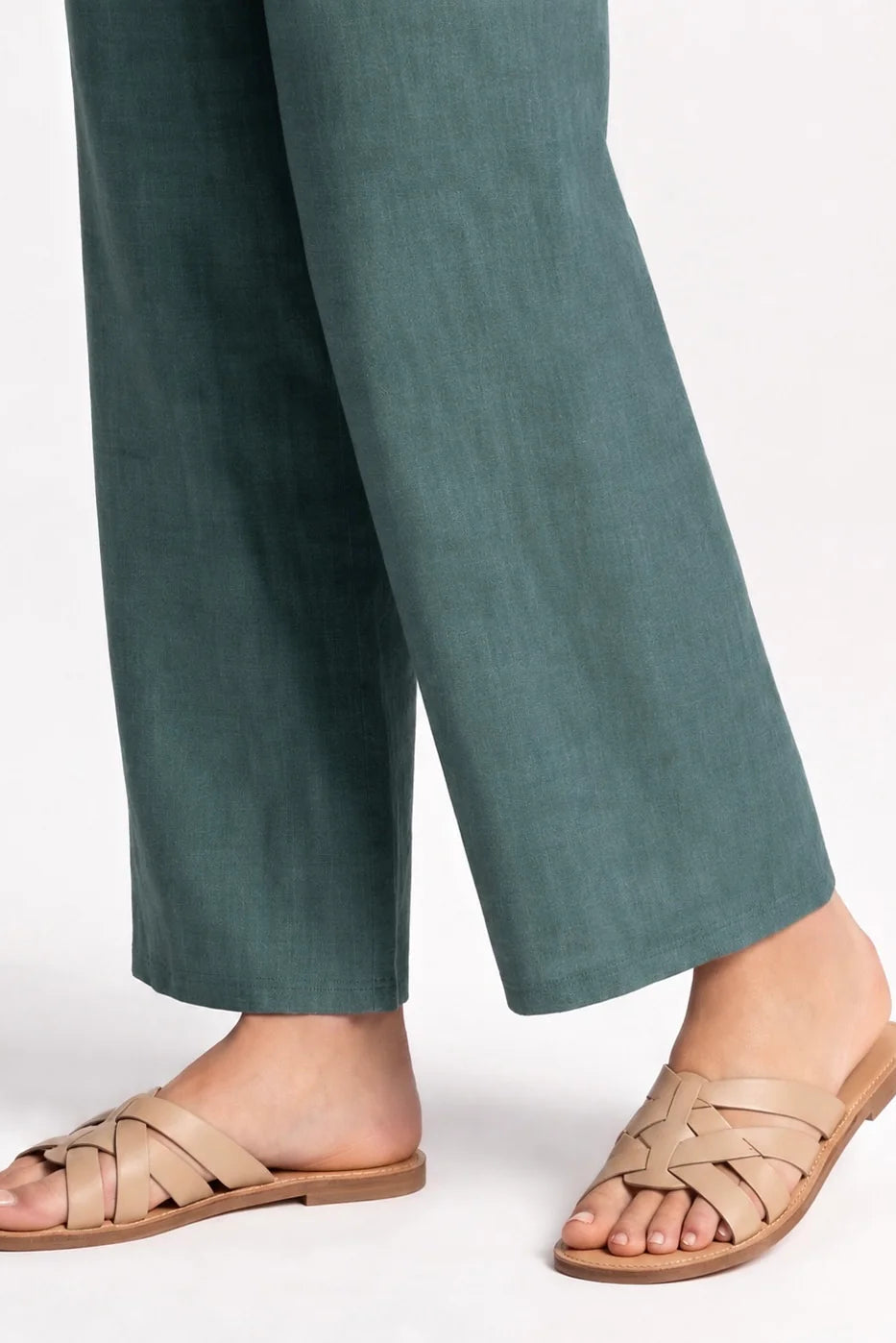 Close up lower leg view of awoman wearing the Kollontai Susan Pants in Green, standing in front of a grey background. 