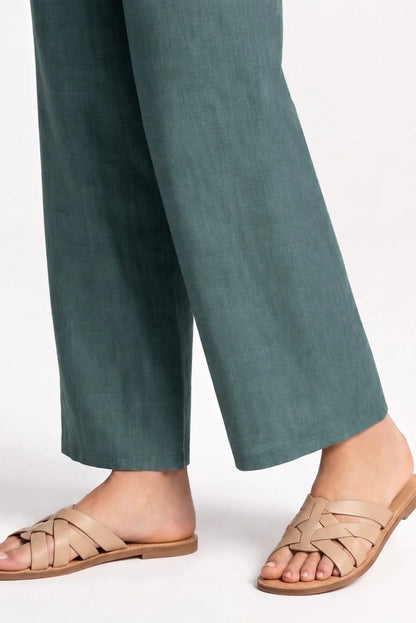 Close up lower leg view of awoman wearing the Kollontai Susan Pants in Green, standing in front of a grey background. 