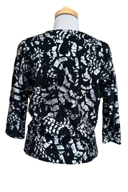 A back view of the Posey Sweater from Compli K in Black and Silver, with a round neck, 3/4 sleeves, and a tie detail at the waist, with black pants, is shown on a mannequin in front of a white background. 