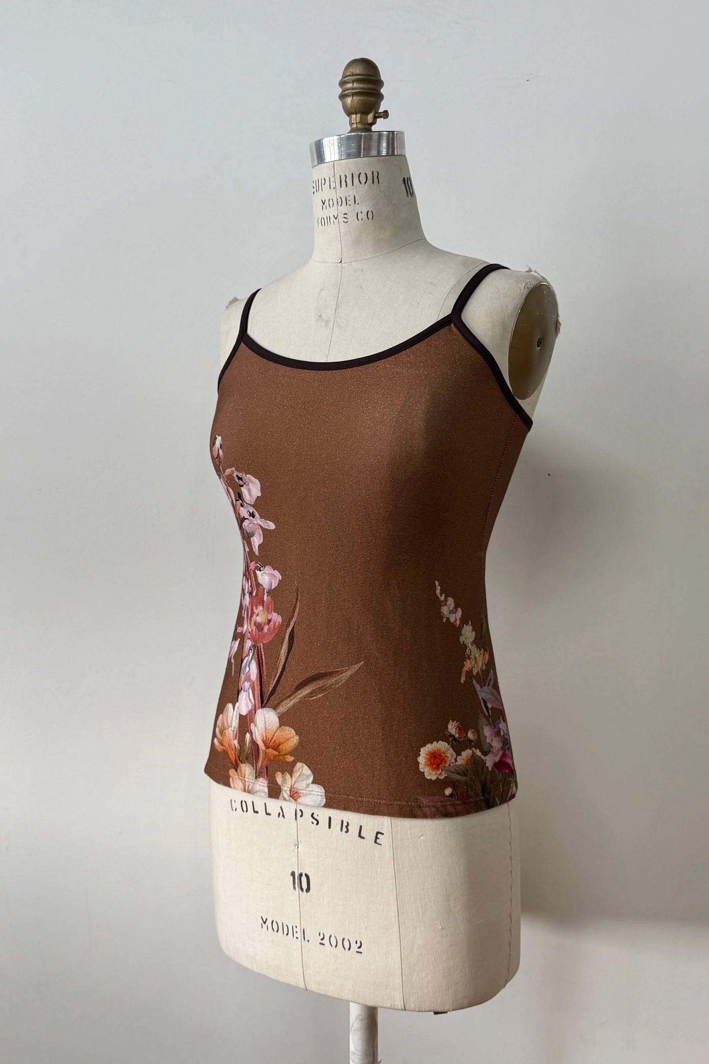 The Morganne Top by Kollontai, a brown floral tank top with spaghetti straps, is shown on a mannequin against a grey background