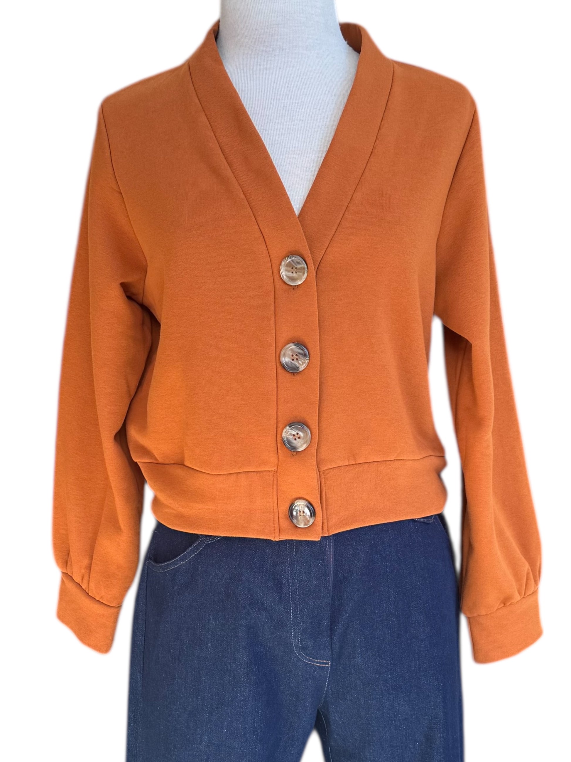 The Douglas Fleece Cardigan by Eve Lavoie in Pumpkin, a short cardigan with tortoiseshell buttons and a wide waistband, is shown with jeans on a mannequin against a white background