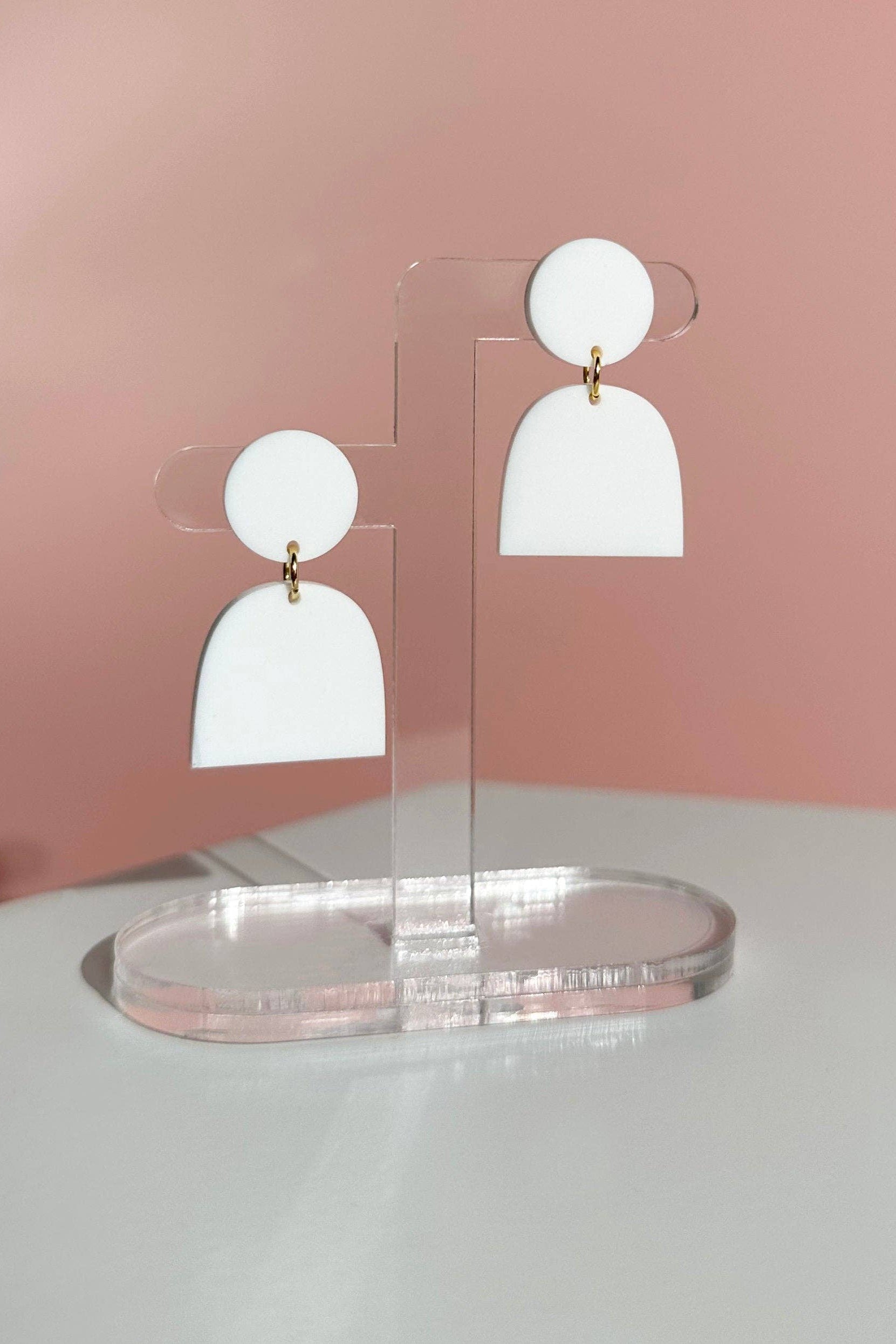 White earrings on a clear stand against a pink background