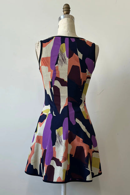 A back view of the Silba 2026 Dress by Kollontai, a sleeveless short dress in a Multicolour abstract print with a fit and flare shape and princess seams, is shown on a mannequin against a white background. 