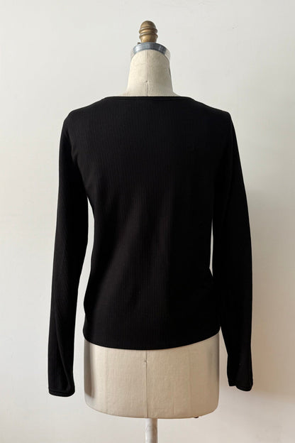 A back view of the Virginia Top by Kollontai in Black, a corduroy-textured top with inverted pleats on the long sleeves, a slim fit and a round neck, is shown on a mannequin against a grey background. 