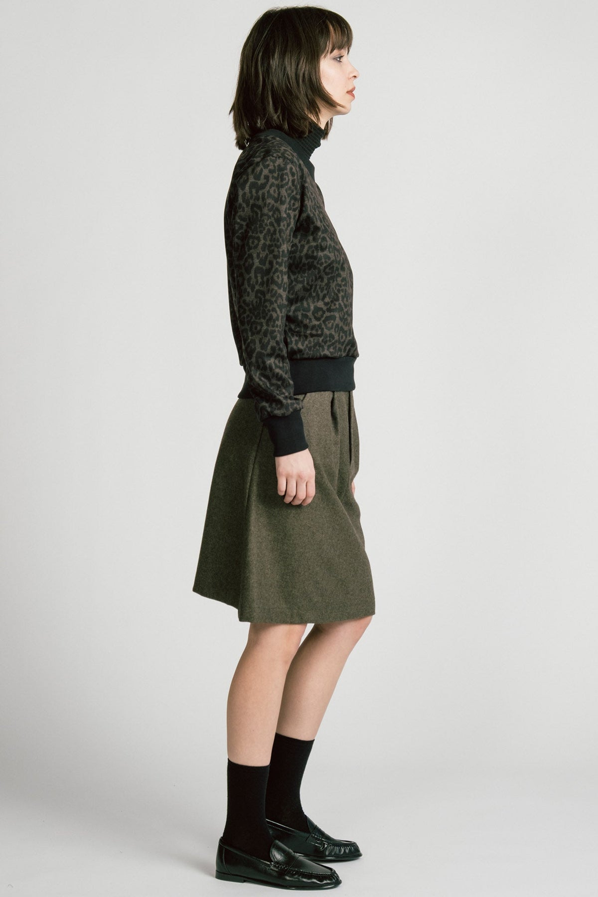 Side view of a woman wearing the Crux Sweatshirt by Allison Wonderland in Animal Print. she is wearing it with a grey skirt and standing in front of a white background. 