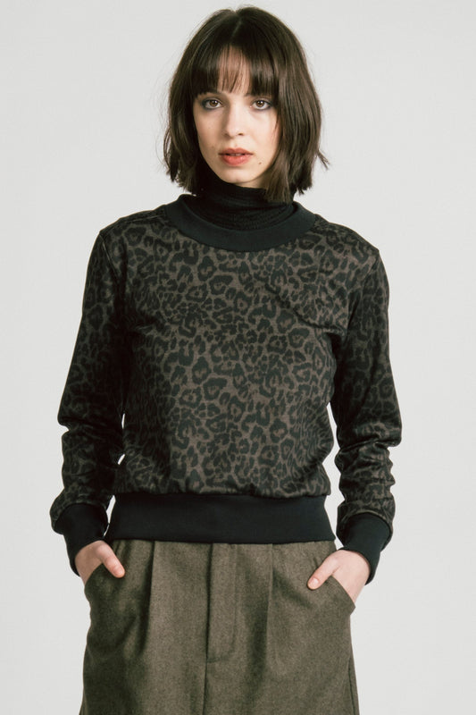 A woman wearing the Crux Sweatshirt by Allison Wonderland in Animal Print. she is wearing it with a grey skirt and standing in front of a white background. 