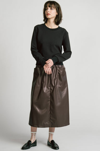 A woman wearing the Crux Sweatshirt by Allison Wonderland in Black Texture. she is wearing it with a brown pleather skirt and standing in front of a white background. 
