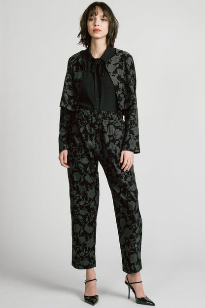 A woman wearing the Libra Bolero by Allison Wonderland in Floral, a dark printed corduroy cropped jacket with a single button closure. She is wearing it over a black top with matching pants. 