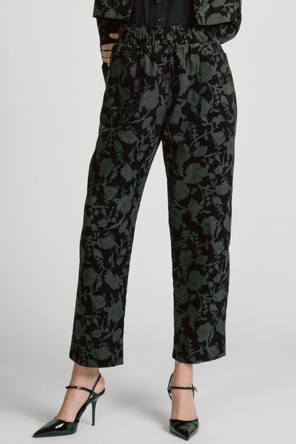 Waist down view of a woman wearing the Orion Pants by Allison Wonderland, relaxed fitting pants with an elastic waist and pockets in a dark Floral print on fine wale corduroy. She is wearing them with the matching Libra Bolero and standing in front of a white background. 