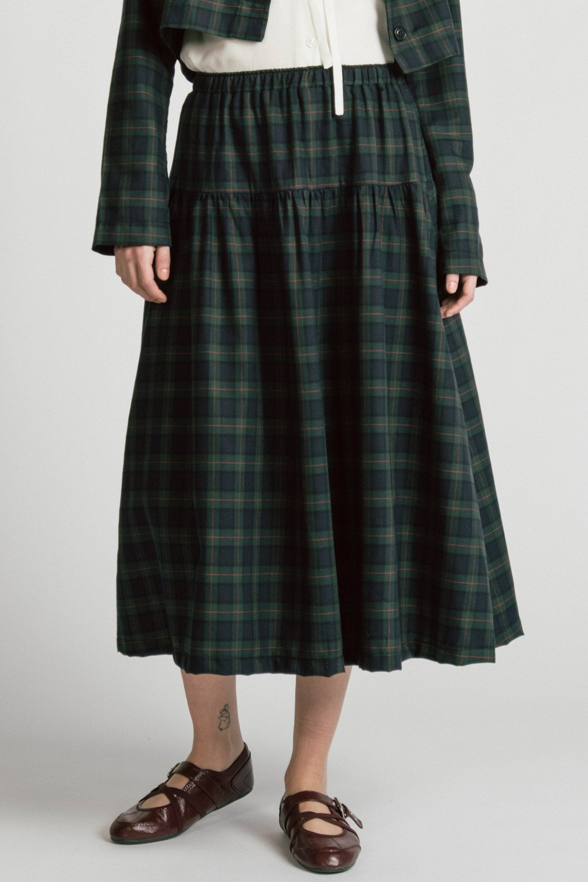 Waist down view of a woman wearing the Pegasus Skirt in Plaid by Allison Wonderland, a midi length A-line skirt with an elastic waist, with the matching Libra bolero and a white top. She is standing in front of a white background