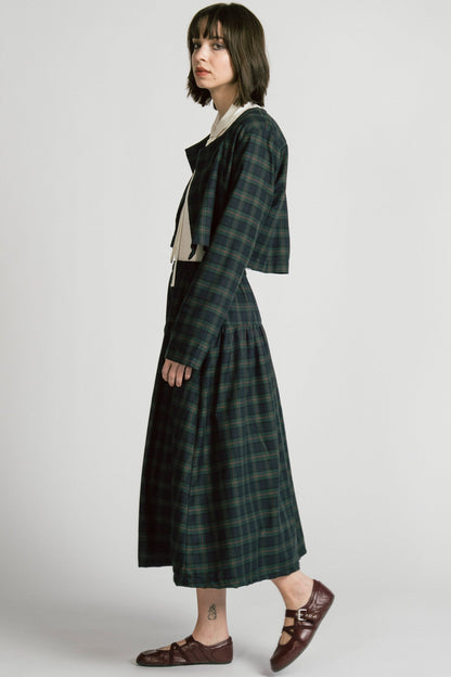 Side view of a woman wearing the Pegasus Skirt in Plaid by Allison Wonderland, a midi length A-line skirt with an elastic waist, with the matching Libra bolero and a white top. She is standing in front of a white background